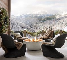 an outdoor fire pit surrounded by chairs in front of a snowy mountain scene with trees