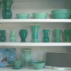 green vases and bowls are on shelves in a room with white shelve