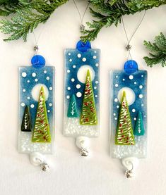 three christmas ornaments hanging from a tree on a white surface with green and blue decorations