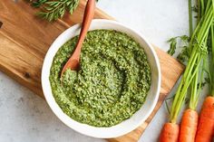 a white bowl filled with pesto next to carrots and celery on a cutting board