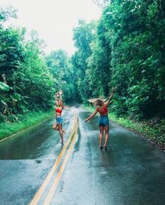 two women in bathing suits are dancing on the road with trees and bushes behind them