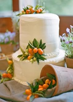 a three tiered white wedding cake with orange flowers on top and greenery around it