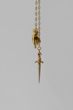 A fixed lariat style necklace made with an 18k gold-filled drawn cable chain with two tiered hanging pendants. An 18k gold filled brass 3D hand pendant with eye emblem and rhinestone cuff playfully hangs just above a sterling silver sword as if the hand is reaching for the sword. This necklace has no closures and easily fits over the head with a 30" neck chain opening. Details: Lariat necklace with dagger & hand pendants 18k gold-filled drawn cable chain - 36" length 18k gold filled brass 3D han Medieval Accessories Jewellery, Hand Cast Gold Sterling Silver Jewelry, Hand Cast Sterling Silver Gold Jewelry, Adjustable Hand Cast Yellow Gold Jewelry, Adjustable Hand-cast Yellow Gold Jewelry, Minimalist Hand Cast Brass Jewelry, Hand Cast Brass Dangle Jewelry, Brass Lariat Jewelry As A Gift, Brass Lariat Jewelry For Gifts