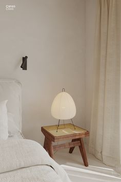 a white bed sitting next to a wooden table with a lamp on top of it