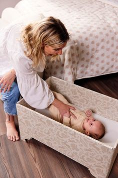 a woman kneeling down next to a baby in a crib that is on the floor