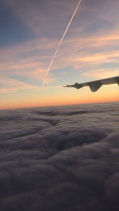 an airplane wing flying above the clouds at sunset