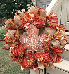 a welcome fall wreath on the front porch with an orange and red bow hanging from it