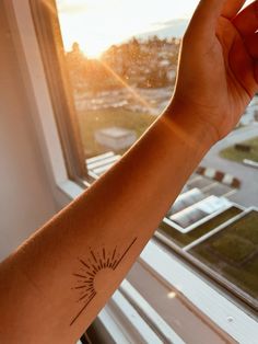 a person's arm with a small sun tattoo on it, in front of a window