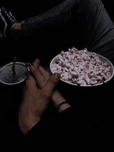 a person sitting in the dark with a bowl of food on their lap and one hand holding a remote control