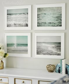 four framed pictures hang on the wall above a white dresser with drawers and vases