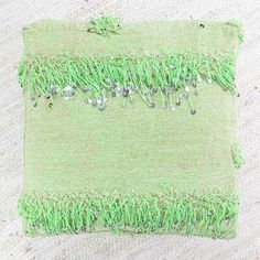 a piece of cloth with green grass and beads on the edges is laying on a white surface