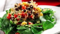 a white plate topped with spinach and black bean salad next to a red pepper