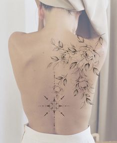 the back of a woman's body with flowers on it and a cross tattoo