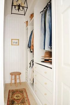 a white closet with clothes hanging on the wall and a rug in front of it