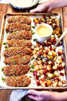 two hands holding a tray with food on it and dipping sauce in a small bowl