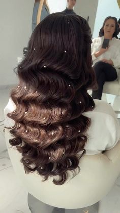 the back of a woman's head with wavy brown hair in front of a mirror