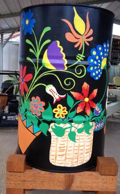 a large black bucket with colorful flowers painted on it's side and wooden stand