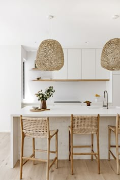 two wicker lamps hanging over an island in a kitchen with white countertops and wooden chairs