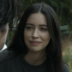 a close up of a person wearing a black shirt and looking at another person in the background