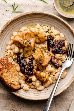 a white plate topped with beans and meat next to a fork on top of a table