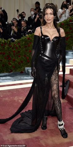 a woman in a black dress and gloves on the red carpet with cameras around her