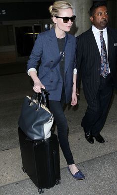 a woman in sunglasses and a suit carrying a black bag