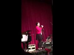 a woman standing on top of a stage next to a piano