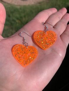 "Each pair of sparkly neon orange heart earrings are handmade to order, therefore no two pairs are identical! However, I try to get as close as possible :) Made with nickel-free & hypoallergenic sterling silver plated fishhook earrings. Hearts are approximately 1.25\", and are made with epoxy resin and neon orange holographic glitter! 🧡 UV blacklight reactive! Perfect for Halloween, concerts, raves, parties, festivals, etc.  Thanks for visiting my shop! ✨" Cute Orange Jewelry For Party, Cute Orange Party Jewelry, Heart-shaped Orange Jewelry For Gift, Orange Heart-shaped Jewelry Gift, Orange Heart Charm Jewelry, Handmade Orange Heart Jewelry, Handmade Heart-shaped Orange Jewelry, Handmade Orange Heart-shaped Jewelry, Earrings Hearts