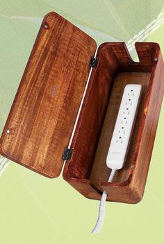 an electronic device in a wooden box on a green and white background with the cord plugged into it