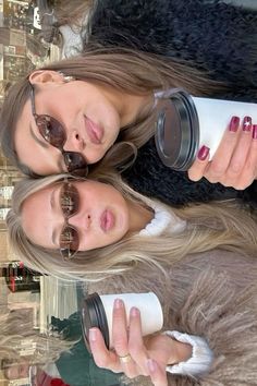 two beautiful young women standing next to each other holding coffee mugs and looking at the camera