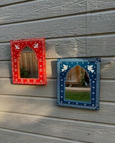 two small mirrors are hanging on the side of a house, one is red and one is blue