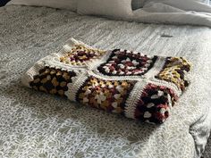 a crocheted blanket laying on top of a bed with white sheets and pillows