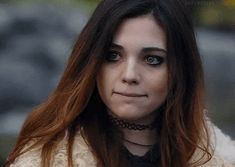 a close up of a person with long hair and wearing a fur coat looking at the camera