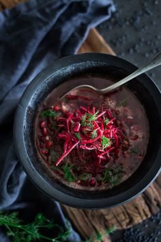 a black bowl filled with soup and garnished with red onions, carrots and parsley