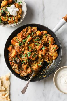 a pan filled with chicken and vegetables next to pita bread on a white table