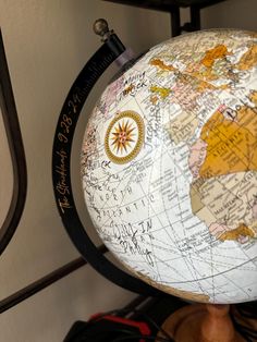 a globe with writing on it sitting on top of a wooden stand next to a wall