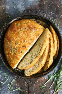 sliced bread in a cast iron skillet with rosemary sprigs on the side