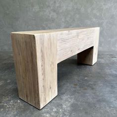 a wooden bench sitting on top of a cement floor in front of a gray wall