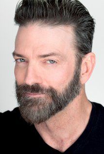 a close up of a person with a goatee and beard wearing a black shirt