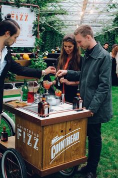 three people standing around a table with drinks on it