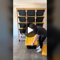 a woman is bending over to pick up some items from a storage area with yellow bins