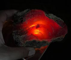 a hand holding a piece of rock with red light coming out of it's center