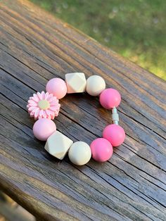 a pink and white beaded bracelet with a flower on the end is sitting on a wooden table