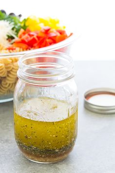 a salad in a glass jar next to a bowl of pasta and dressing on a table