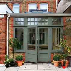 an orange brick building with green double doors and potted plants in the foreground