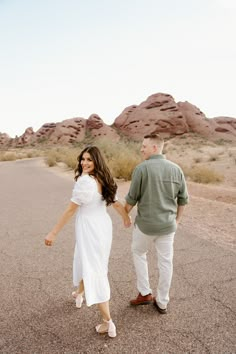 a man and woman holding hands while walking in the desert