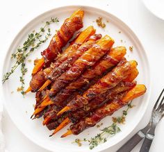 bacon wrapped carrots on a white plate with fork and knife next to the plate