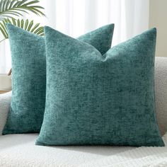 two green pillows sitting on top of a white couch next to a potted plant