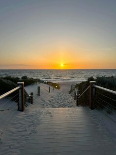 the sun is setting over the ocean and beach with stairs leading to the beach area