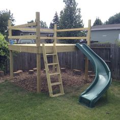 a green slide in the grass next to a wooden fence